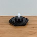 Black decorative candle holder with a white candle on a wooden surface